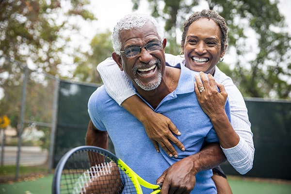 Old couple playing tennis while smiling for their new teeth