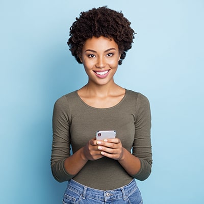 A woman with porcelain veneers smiling while using her phone