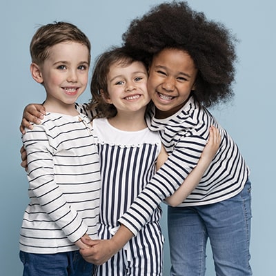 Three five year old children hug each other while smiling