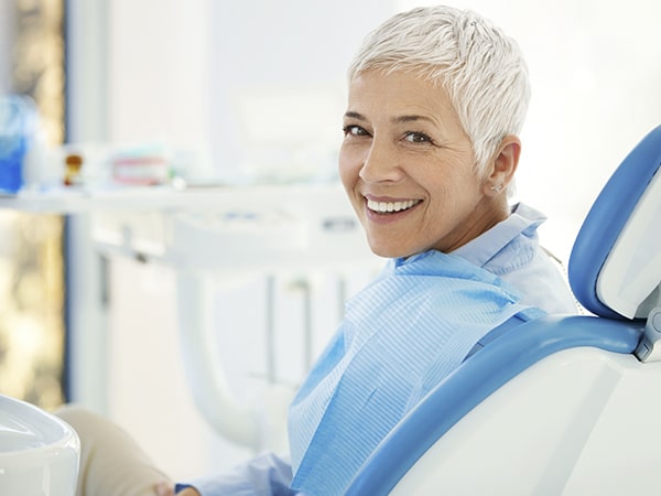 A mature woman sitting in the dentist's chair while smiling